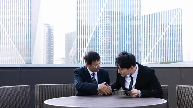 Finishing up a meeting two businessmen shaking hands after successful deal negotiation, good deal of trading to sign agreement, negotiation or property development deal on modern rooftop terrace
