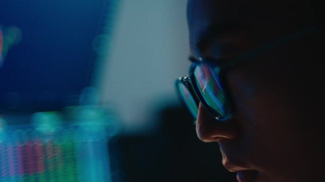 A cinematic close-up shot of a trader's face in profile, showing intense focus as financial charts and glowing data are reflected in his glasses during a late-night session