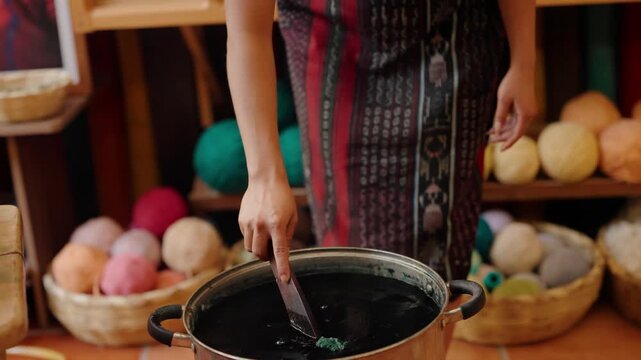 Textile artisan stirs dark dye bath for handmade yarn