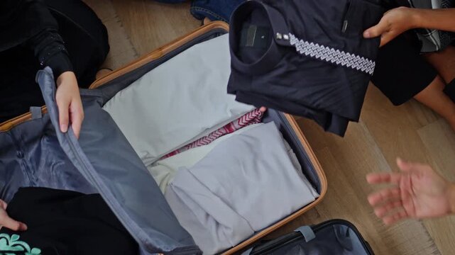 Top view of hands organizing suitcase with hijabs, koko shirts, and prayer rug for Eid Mudik journey