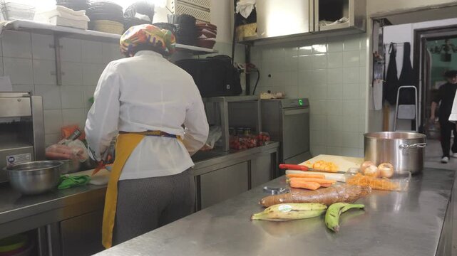 African women chefs work in a professional kitchen preparing cassava (Manihot esculenta), plantain (Musa spp.), carrot (Daucus carota), onion (Allium cepa) and yam (Dioscorea spp.) beside a stock pot