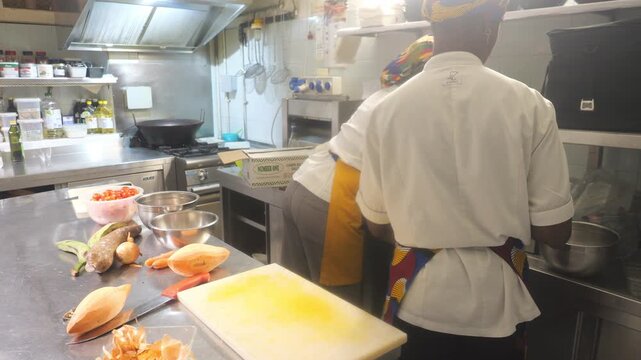 African women chefs prepping cassava, yam and vegetables with knives in professional kitchen workspace