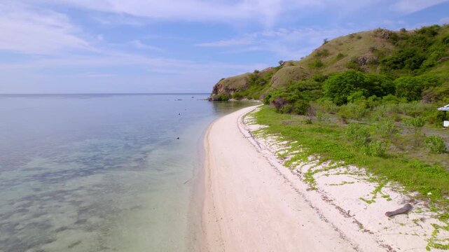 Aerial view of young man and woman having a stroll on untouched white-sandy shoreline along turquoise waters of Kanawa Island, Indonesia.