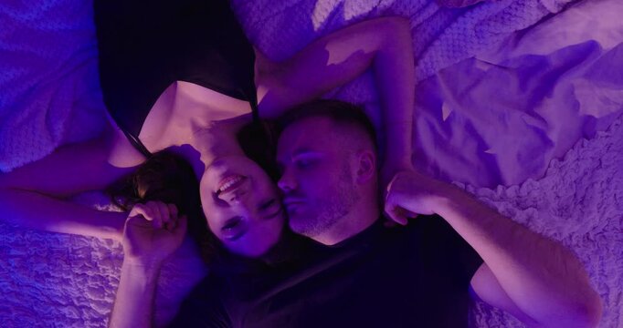 Overhead cinematic shot of a couple lying close together in bed under soft colored lighting. Concept of love, intimacy, emotional connection and romantic relationship.