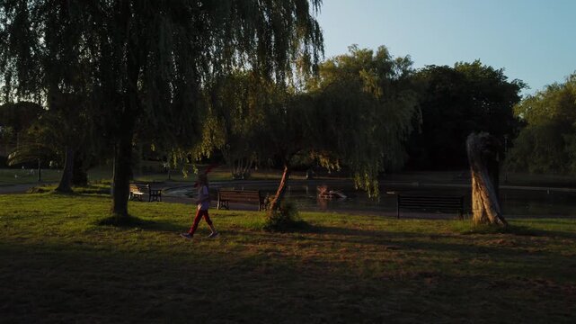 Cinematic golden hour footage of a girl walking through Victoria Park, Paignton. Beautiful sunset light filters through willow trees by the pond in Devon, UK.