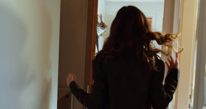 Indoor back view of a woman putting on a leather jacket and walking out the door. Concept of independence, decision, lifestyle movement and everyday departure scene.