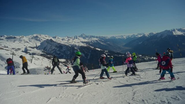 Atmospheric shot of skiers and snowboarders gathering at the top of the ski lift in Anz&egrave;re. Relaxed alpine mood, panoramic Rhone Valley views, bluebird winter light, and authentic resort lifestyle sce
