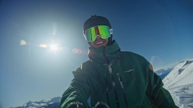 Portrait shot of a very happy person at the top of a ski slope in Anz&egrave;re, Swiss Alps, playfully spraying snow between their hands with a big smile. Bright bluebird light and joyful alpine winter atmos