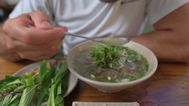 Person Delicately Tastes Traditional Soup. Individual Slowly Savors Genuine Broth And Herbs. Casual Restaurant Scene With Customer Leisurely Enjoying And Savoring Traditional Vietnamese Pho