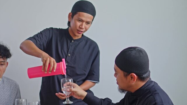 Two Muslim men sharing drink at dining table during Ramadan Iftar or Eid celebration