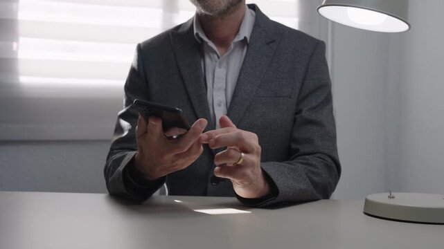 Unrecognizable businessman types on smartphone and then places it face down on desk. Concept of ending conversation, decision made, focus, boundaries and corporate workflow.