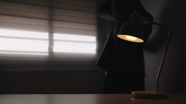 Warm desk lamp in dark office before window blinds open and natural light floods the room. Concept of clarity, solution, optimism and new beginning in business environment.