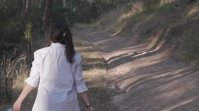 A young woman collects trash while walking along a nature trail at Warrendyte Park, Melbourne. Captured during evening twilight, the scene showcases serene, natural beauty and eco-friendly action.
