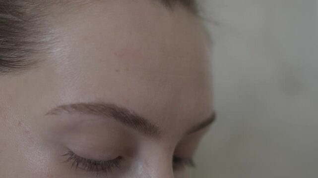 Close up of adult woman grooming eyebrow with makeup brush indoors