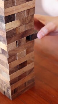 Vertical Close Up of Hand Removing Block from Wooden Tower