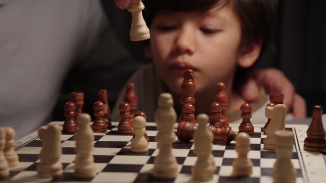 Close view of child watching as father decisively captures his queen, knocking pieces over. Boy reacts surprised and smiling. Concept of strategy, learning and mentorship.