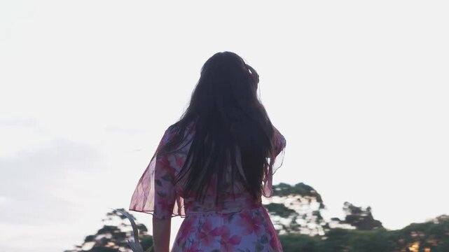 A young Hispanic girl wearing a floral dress walks in Croydon Park, Australia, during sunset. The warm hues of twilight enhance the serene outdoor atmosphere, captured in a medium shot.