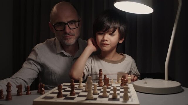 Boy playing chess with his father at home. Child makes checkmate and father reacts surprised, then proud. Concept of learning, strategy, family bonding and childhood achievement.
