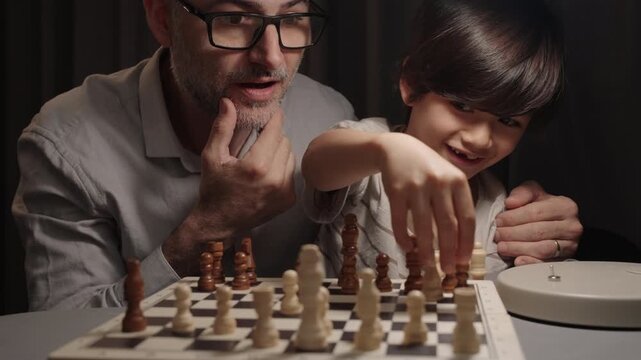 Father reacts with surprise as his son captures a chess knight and smiles proudly, making eye contact. Concept of learning, confidence, family bonding and childhood achievement.