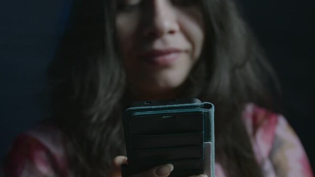 Intimate close-up shot of a young girl smirking while engaging with her smartphone. Dim lighting creates a subtle, mysterious mood. Focused on the face and device, conveying intrigue.