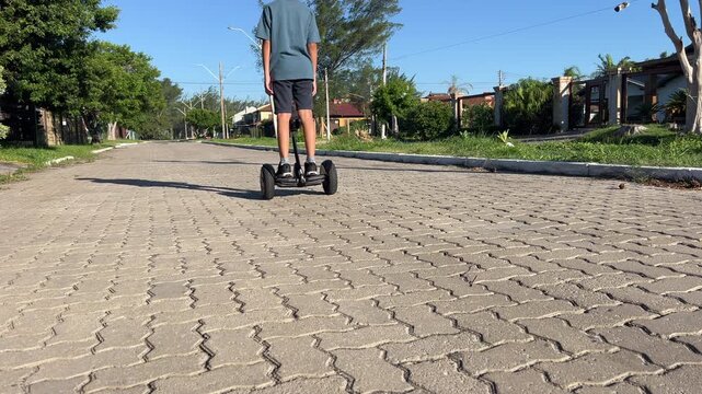 Teen boy steps onto hoverboard and rides away down residential street, starting with board alone in frame, low angle wide shot, 4K30.