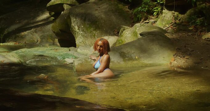 Bright, saturated colors showing a redhead in a sapphire blue bikini posing against the white foam of a cascading waterfall.