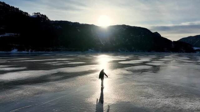 Drone shot flying parallel to ice skater on frozen fjord on scenic winter morning in Norway, slow arc to front of skater.