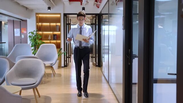 Successful businessman in a formal suit with high spirits looking at documents and answering the phone walks confidently through a modern office hallway