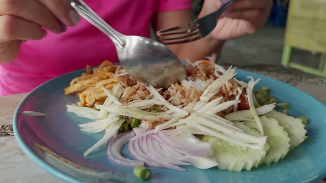 Close up of Khao Khluk Kapi, traditional Thai shrimp paste fried rice served with fresh vegetables, egg strips and side ingredients at local street food market in Thailand.