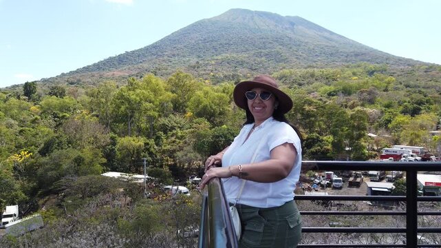 Female traveler at lookout over flowering landscape with Chaparrastique Volcano, San Miguel, El Salvador