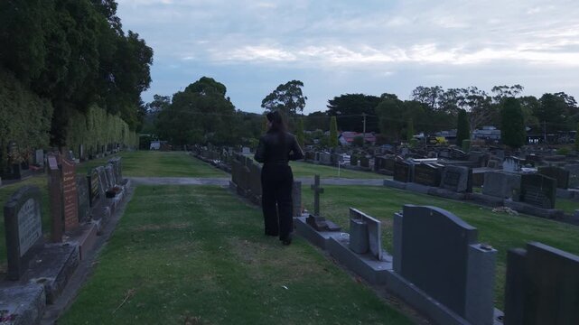 A woman walks through a serene graveyard in Ferntree Gully, Melbourne, under a setting sun. The peaceful atmosphere is captured in a dynamic, following shot with natural lighting.