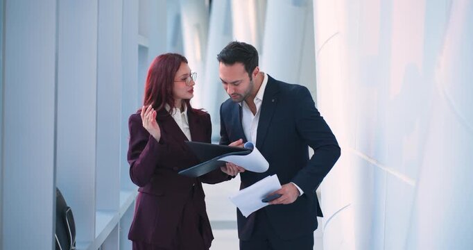 Diverse professional partners examining project folder and discussing strategy in white office space