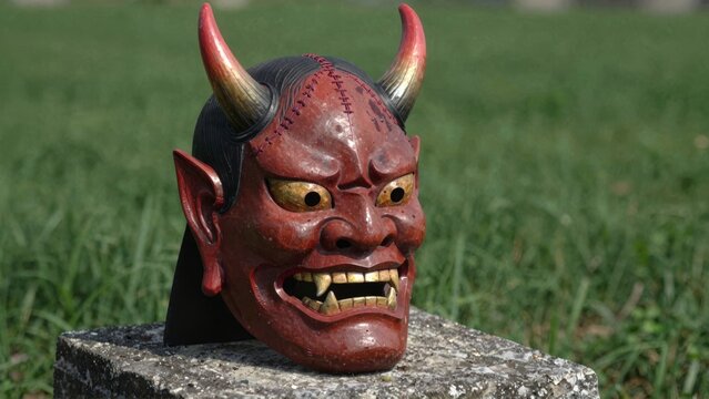 Red demon mask with horns on stone in grass