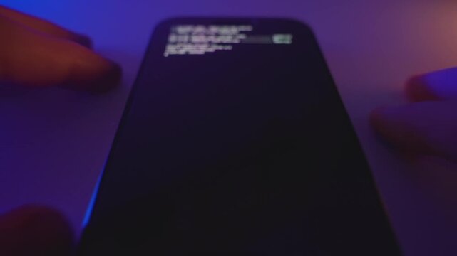 Smartphone screen display code or program installing malware or spyware on device in dark room. Person or hacker spy downloading or uploading software to gather information tracking cyber activity