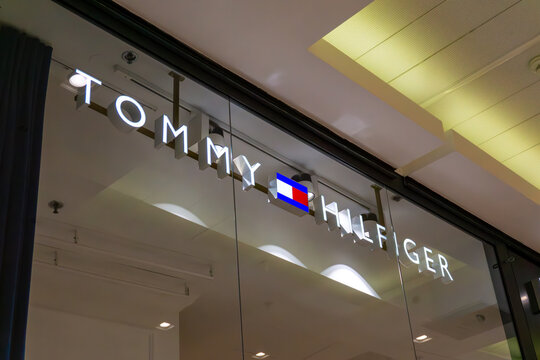 Elegant illuminated Tommy Hilfiger sign in shopping mall, luxury fashion brand logo on glass storefront, modern boutique branding, professional premium retail interior photography, 3D commercial adver