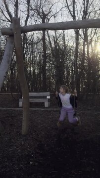 Handheld vertical 9:16 shot of a girl on a swing in Normafa forest. Natural color grade and sharp golden hour light in a 2026 style.