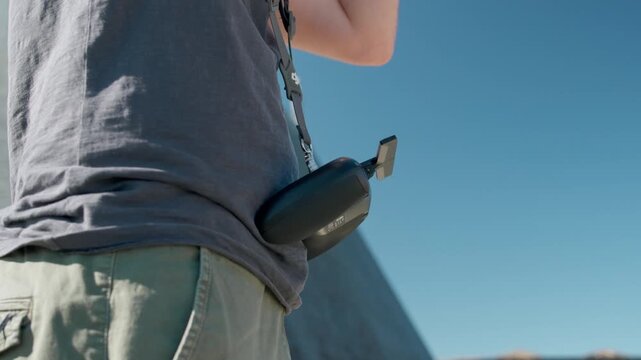 Drone operator standing outdoors with video goggles hanging from a strap around the neck ready for piloting.