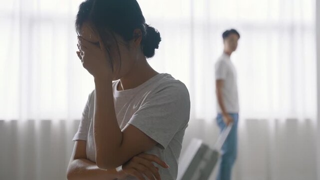Stressed young couple divorce decree, relationship problems crisis conflict, woman crying sadly, male packing clothes and stuffs in trolley luggage ready to leaving home in family conflict concept