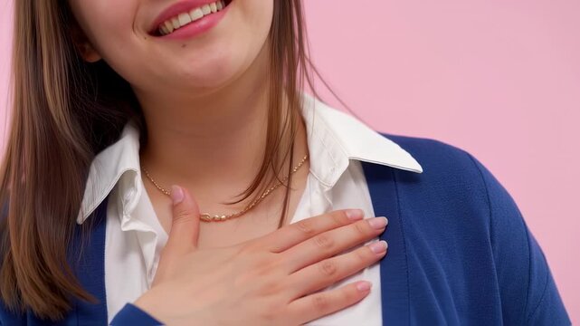 Close-up of a woman's smiling face and upper body, wearing a white collared shirt and a dark blue jacket. A gold chain necklace is visible around her neck.  Her hands are placed