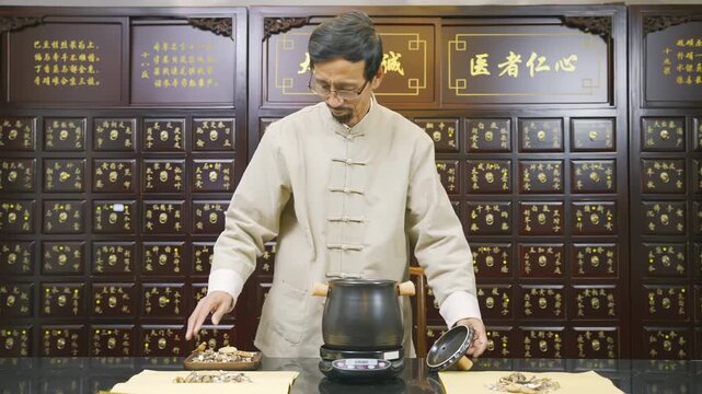 An elderly herbalist apothecary medicine doctor hands adding herbal ingredients to an enamel steaming pot to decoct herbal medicine. Natural remedy and alternative healthcare concept