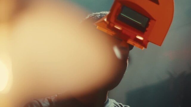 Mechanic wearing welding helmet looking down preparing for metal work, using hammer to hit and mold pieces, slow motion medium