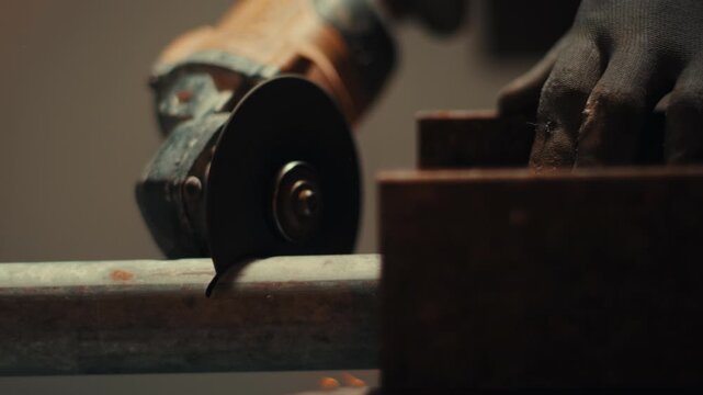 Close up of angle grinder cutting metal pipe on workshop workbench, slow motion precision tool work