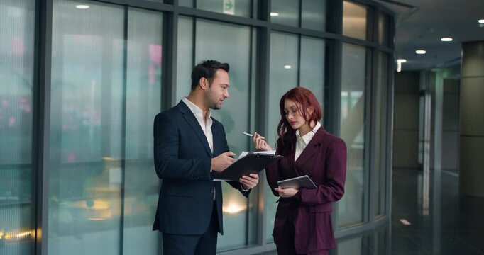 Dissatisfied businessman blames woman colleague for bad project outcomes they argue intensely reviewing documents clipboard tablet in modern corporate hallway slow motion