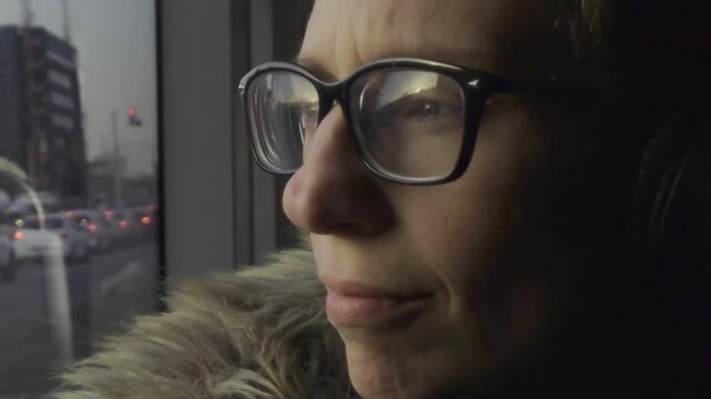 A static shot captures a person wearing glasses and headphones, sitting on a moving tram in Budapest, with the city scene reflected in the window.