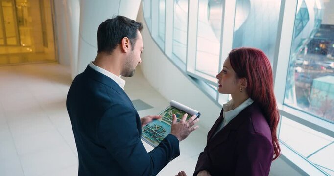 Two architects in friendly mood point at and discuss design improvements on villa concept rendering and building sketch drawings in modern lobby