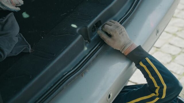 Close up of gloved hand pressing car trunk latch on vehicle rear while working outdoors