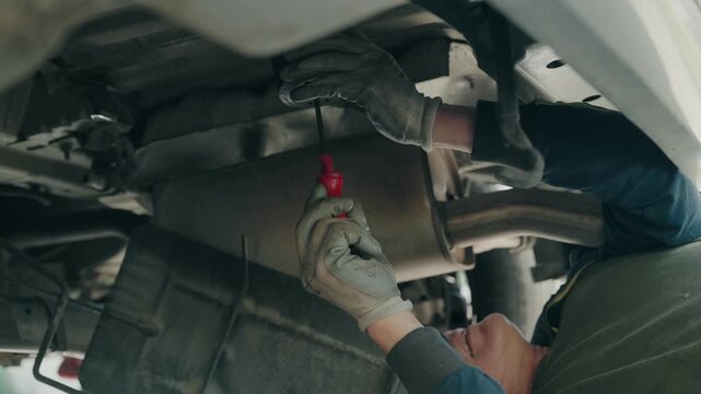 Mechanic using screwdriver under vehicle chassis tightening metal component on car undercarriage during maintenance
