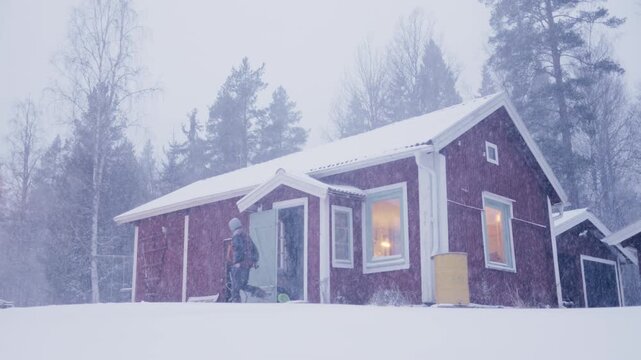Man exits traditional red Swedish house into cold blizzard conditions in winter