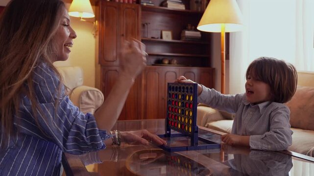 Happy mother and her cute son playing an educational board game at home. The little boy wins and joyfully gives his mom a high five