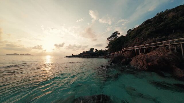 Fast cinematic FPV drone footage cruising low over the sandy coastal beach and ocean waves of Redang Island during a beautiful golden sunrise